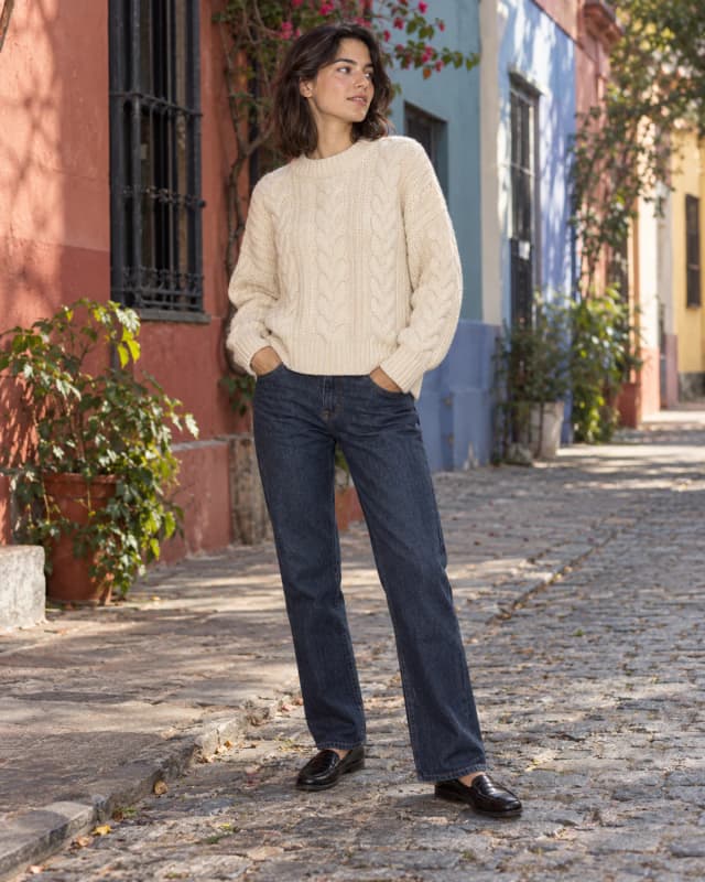 Mujer con suéter tejido crema caminando por una calle con casas de colores