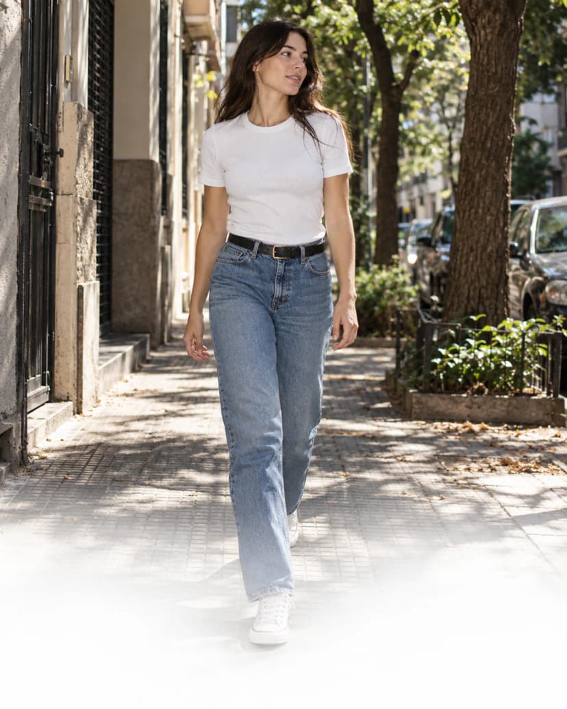 Mujer con remera blanca y jean caminando por la calle